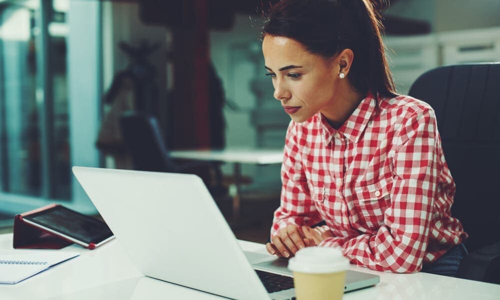 Woman in red and white plaid button down shirt researching tummy tuck with lipo options on her office computer.