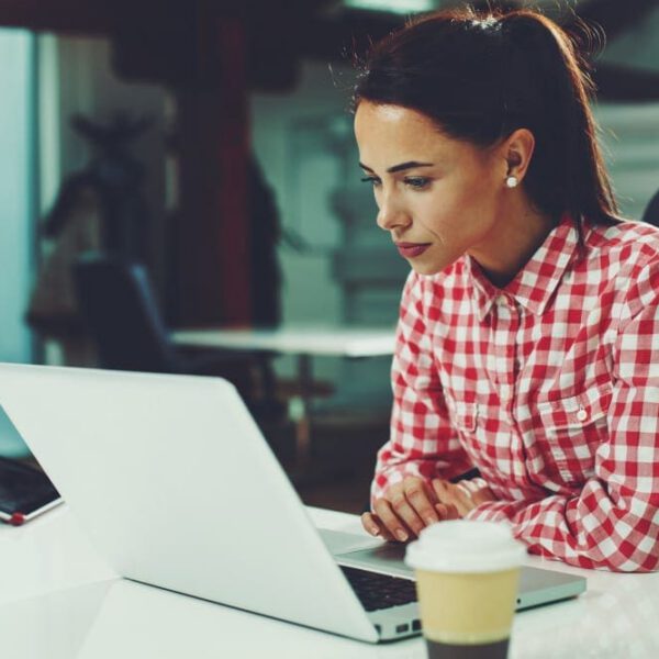 Woman in red and white plaid button down shirt researching tummy tuck with lipo options on her office computer.
