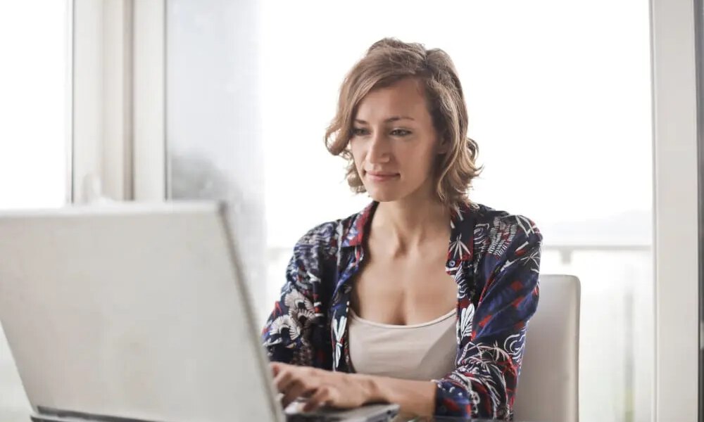 Woman in blue floral top sitting while using laptop.