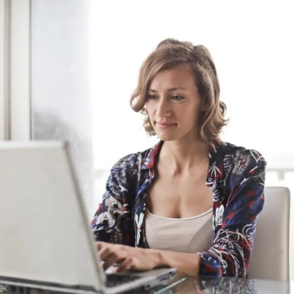 Woman in blue floral top sitting while using laptop.