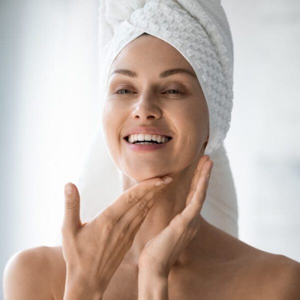 Happy woman with her hair wrapped in a towel looking at her liquid facelift results in the bathroom mirror.