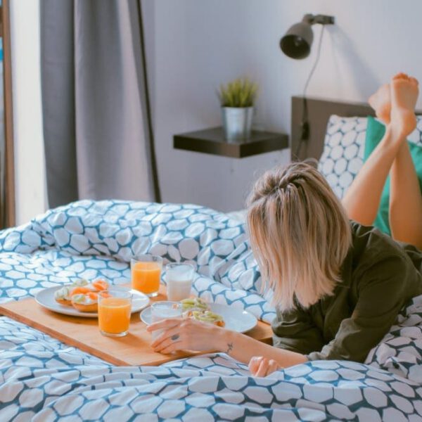 Woman relaxing on her bed while eating from a food tray.
