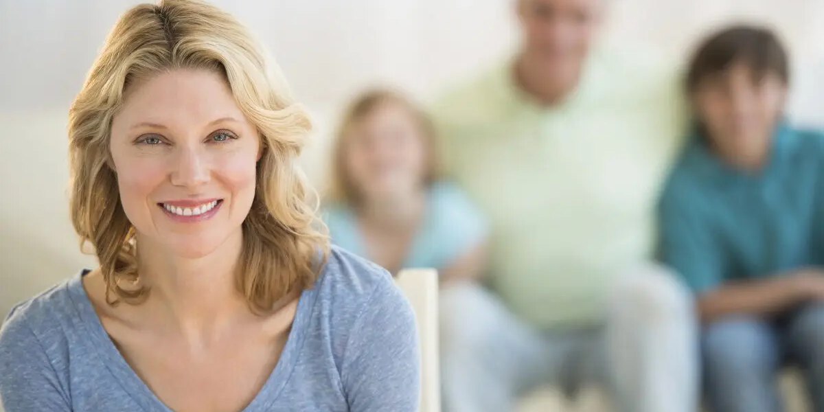 Woman With Family Sitting On Sofa In Background At Home
