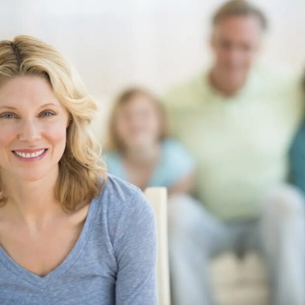 Woman With Family Sitting On Sofa In Background At Home
